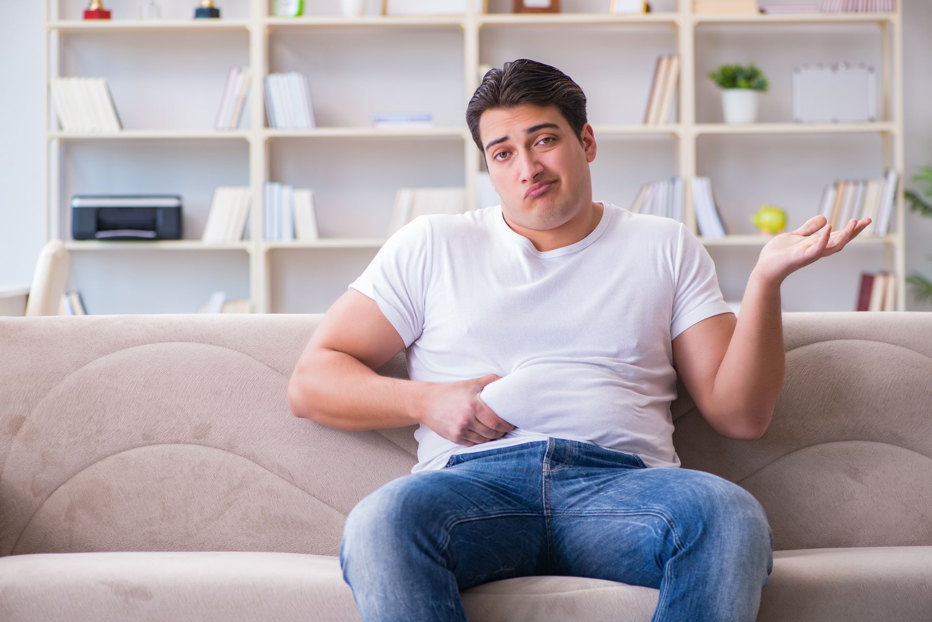 Mężczyzna z nadwagą trzymający się za brzuch i siedzący na kanapie