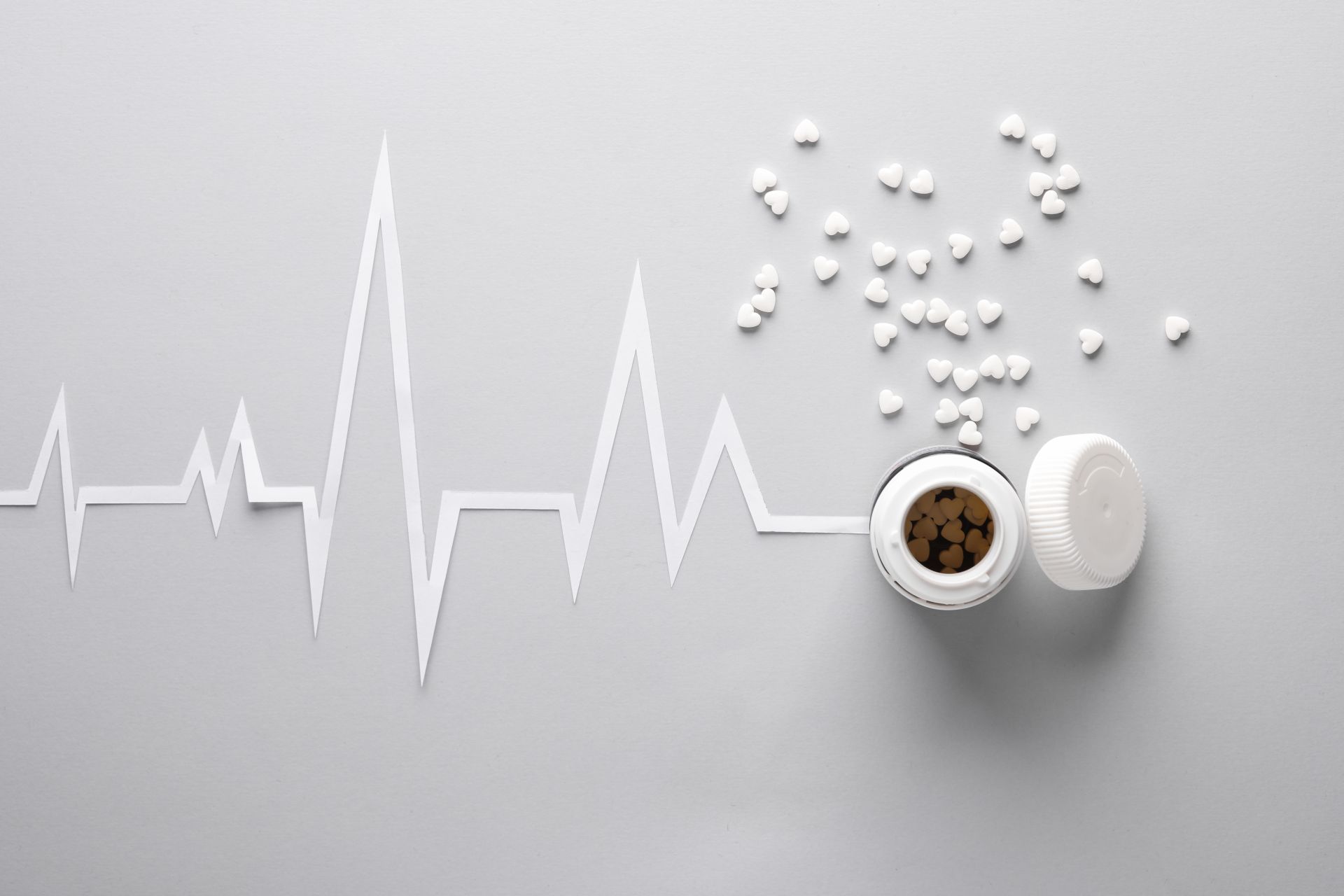 EKG rytmu serca wycięty z papieru, z rozsypanymi tabletkami w kształcie serca obok